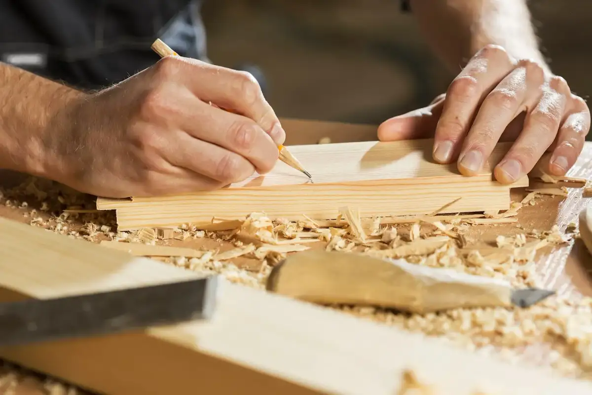 Carpenter marking measurements on a wooden board in a workshop